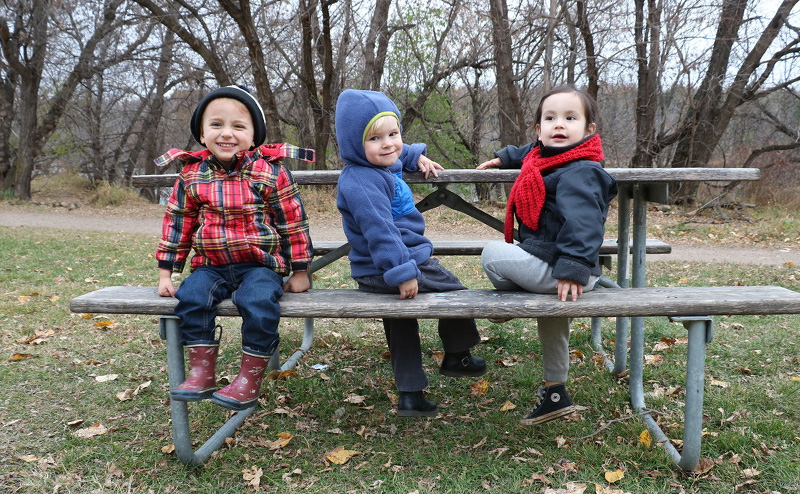 Three kids in warm clothes sitting on a park bench.
