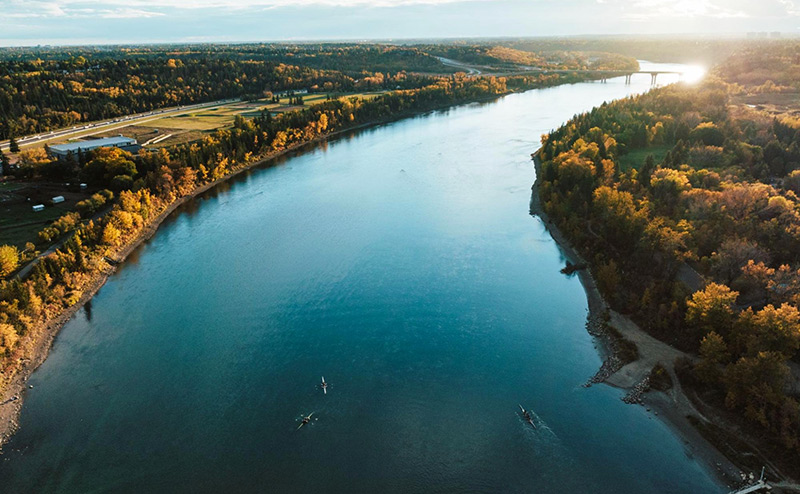 Aerial view of the frozen North Saskatchewan River in winter. The Edmonton skyline is present in the background.
