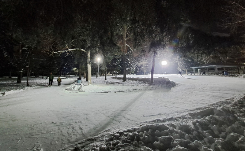 People skating at Rundle Park after dark. The area is illuminated by bright lights.