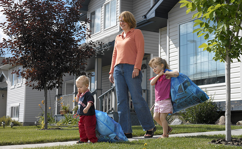 A mom and her kids bringing their blue bags to the curb.