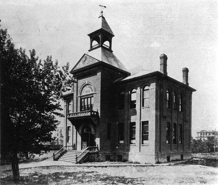 Black and white photo: a large two-story building with a set of stairs at the front entrance.