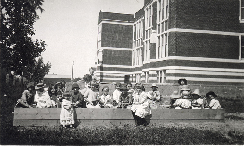 Black and white photo. A group of children playing in a sandbox.