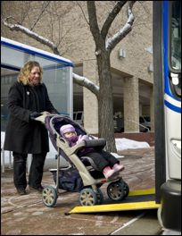 Woman pushes a stroller with a child up a lowered bus ramp