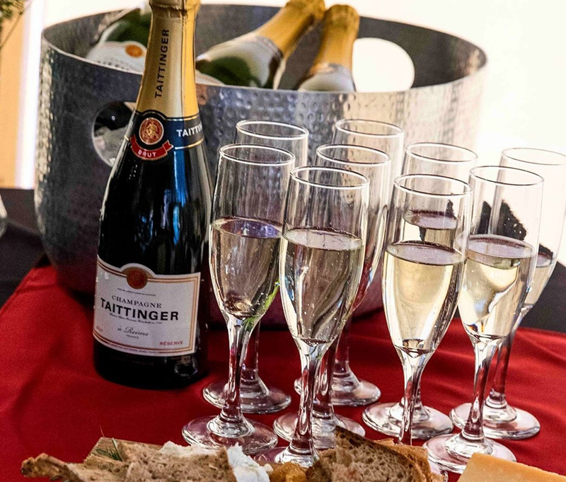 Photo of champagne and champagne glasses on a table. Various breads and cheeses are displayed in the foreground.