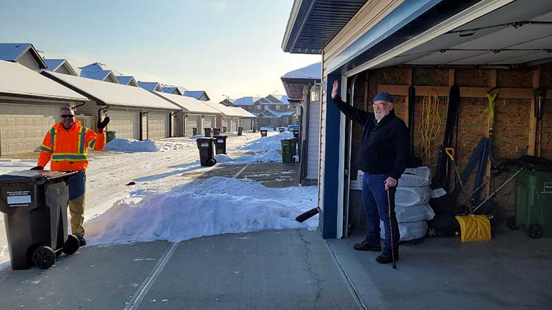 Waste collector pulls a resident's cart to the end of their driveway for collection.