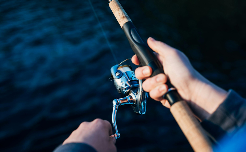 Closeup view of a person's hands reeling in a fishing rod.