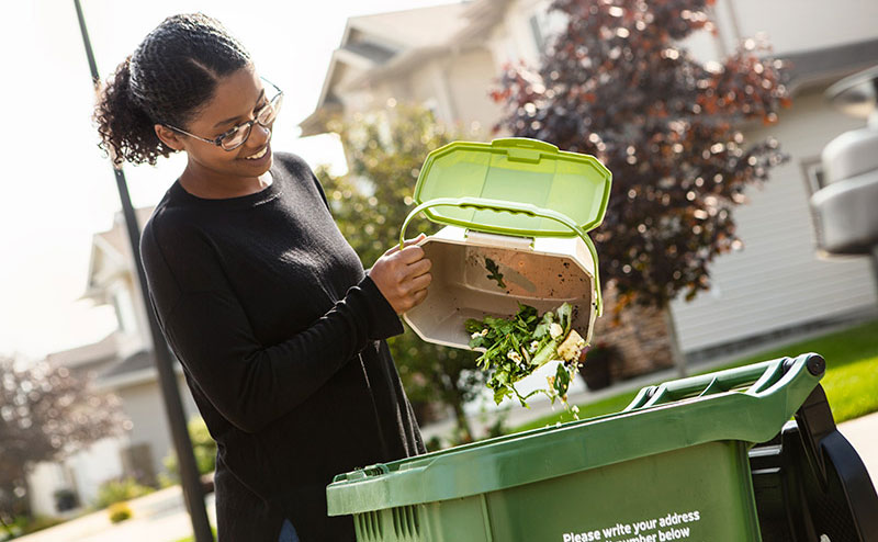 A woman emptying food scraps into a green compost bin.