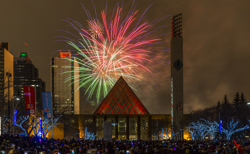 A crowd of people watching a fireworks display near City Hall.