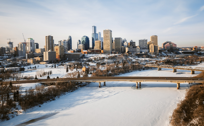 Aerial view of the frozen North Saskatchewan River in winter. The Edmonton skyline is present in the background.