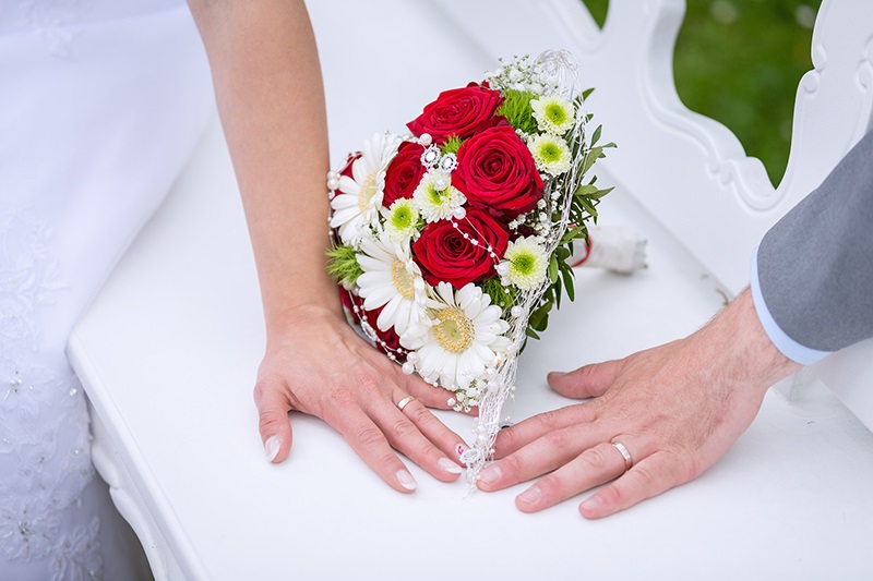 A man and woman's hand with wedding rings on and a bouquet between them.