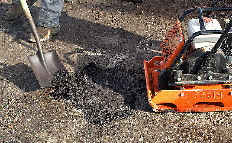 Closeup of a pothole being filled and a tamper machine