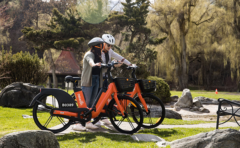 Two riders pushing Neuron e-Bikes through a park