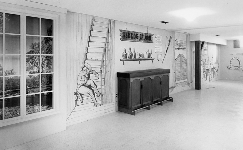 Black and white photo of a basement with walls painted in a western theme.