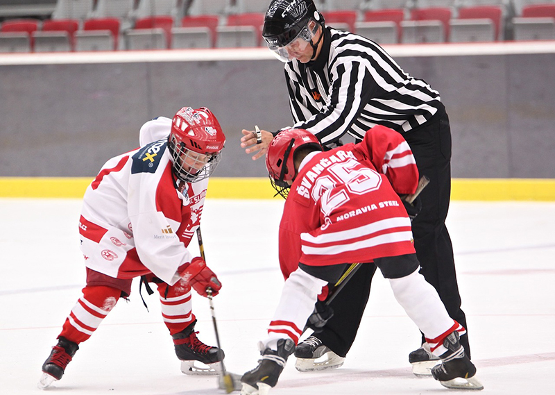 Referee dropping a puck for two young player during face-off