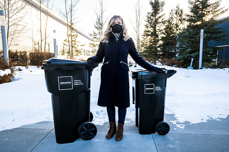 woman standing between two garbage carts
