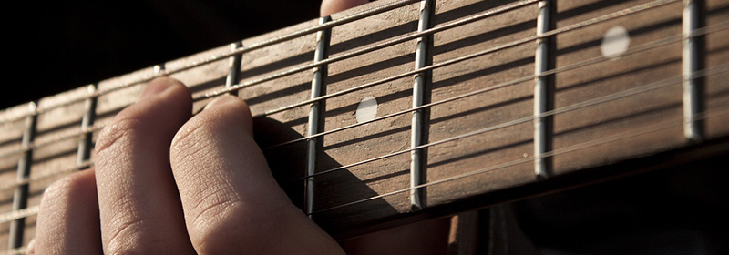 Close up of a person's hand on the neck of a guitar