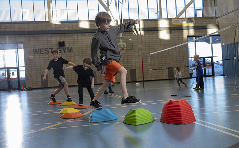 Kids playing a balancing game in a gymnasium.