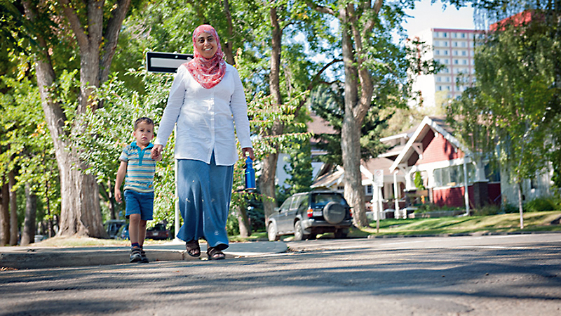 Woman walking with a child on a sidewalk in summer.