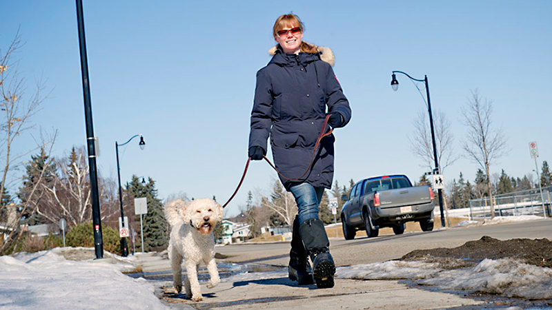 Woman walking a dog on a sidewalk in winter.