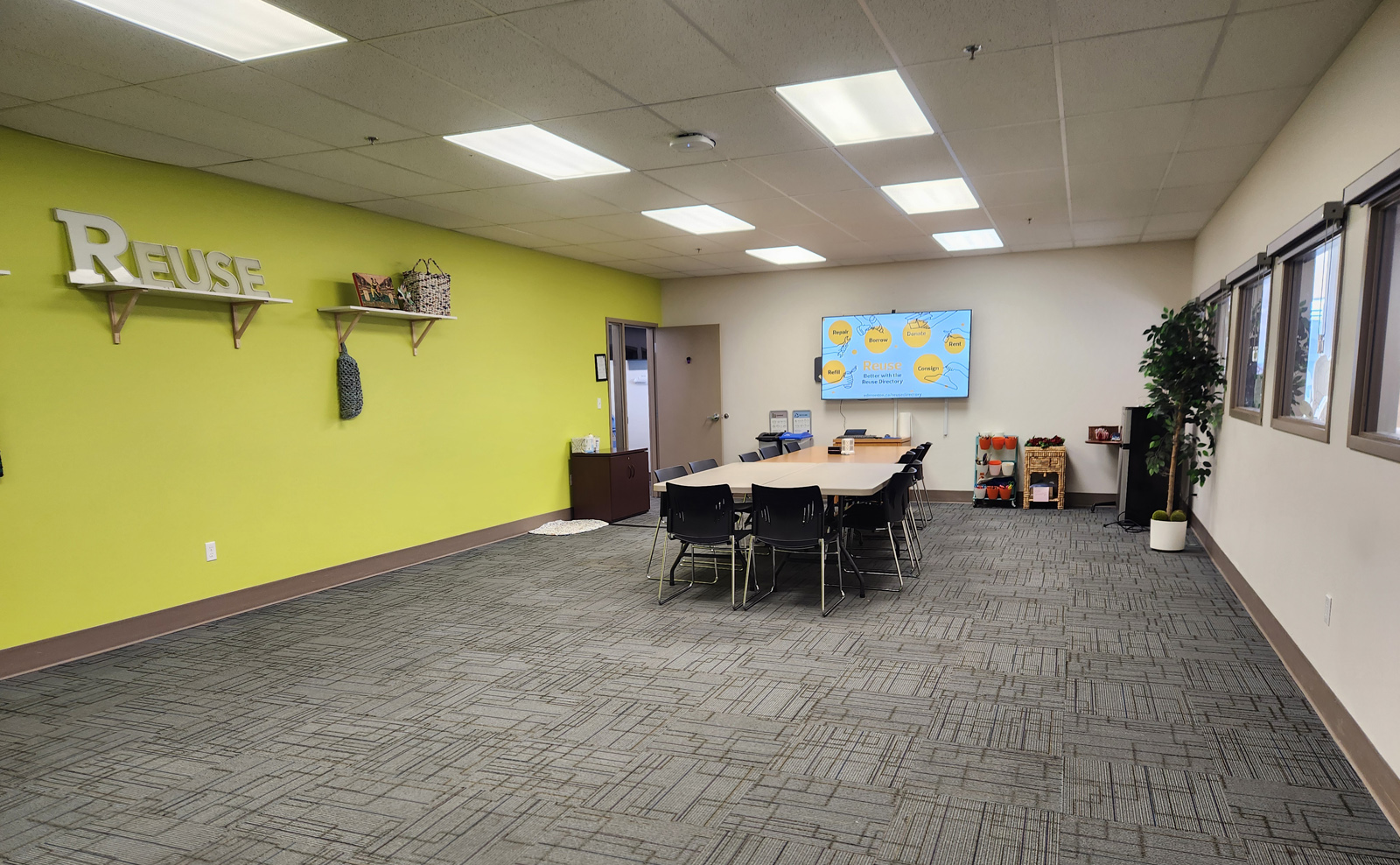 Reuse centre program room, with a long table surrounded by chairs, and a wall-mounted TV screen on one end.