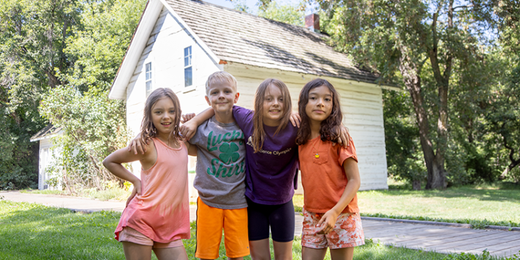 four kids standing in front of white older house