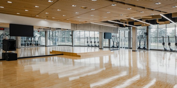 Fitness studio with a large open area, and many workout machines along a large window.
