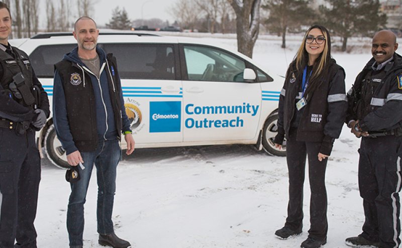 four diverse peace officers standing in front of car marked "Community Outreach"