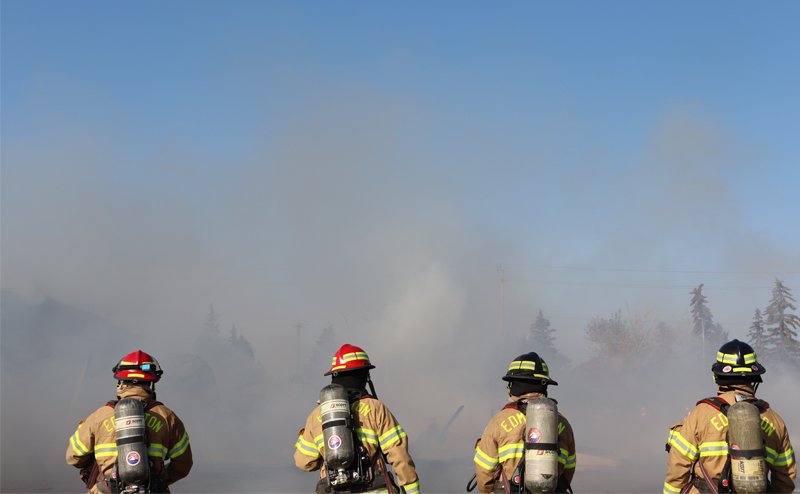 4 firefighters in gear looking at smoke from fire