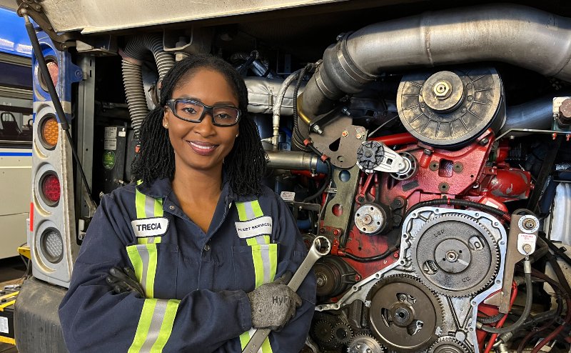 Heavy equipment technician holding wrench in front of transit bus engine
