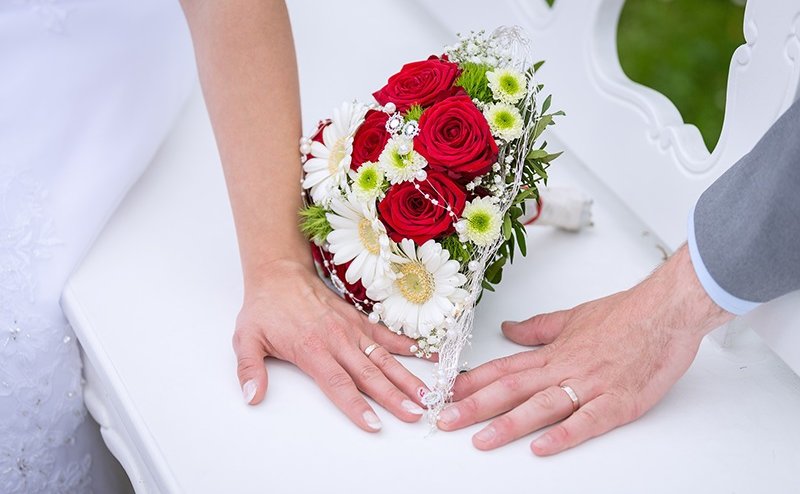 A man and woman's hand with wedding rings on and a bouquet between them.