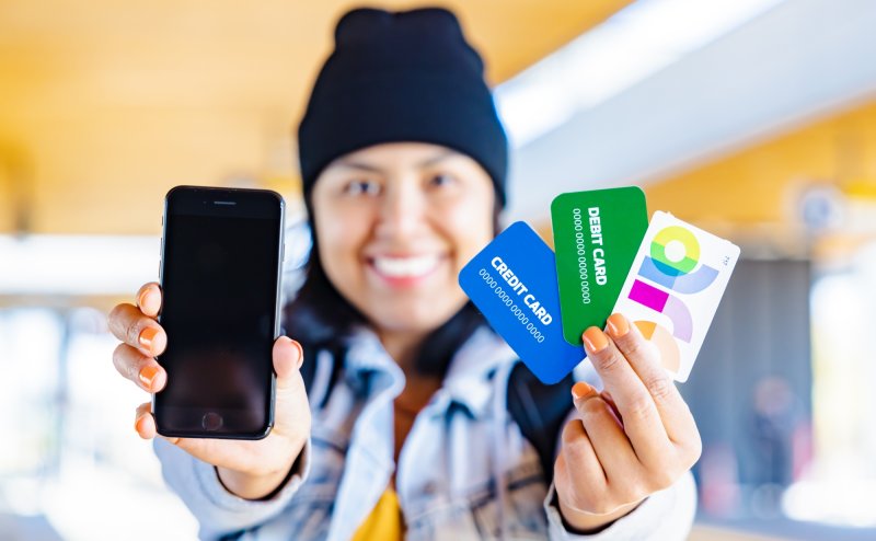 Person smiling, showing a phone, arc card, debit and credit card. 