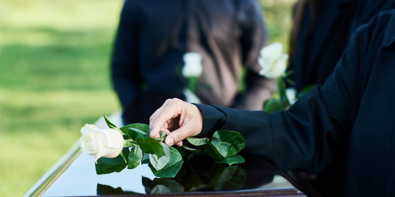 hand putting rose on casket