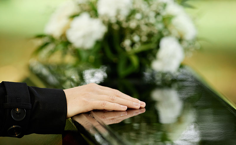 hand on top of casket with white rose