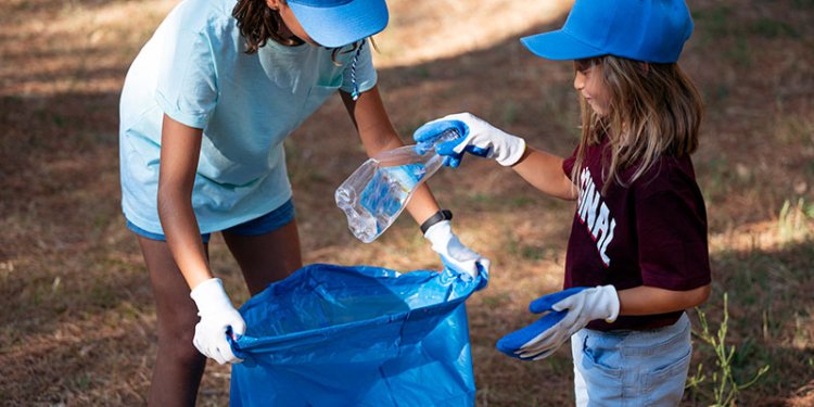 two kids putting plastic bottle in recycle blue bag