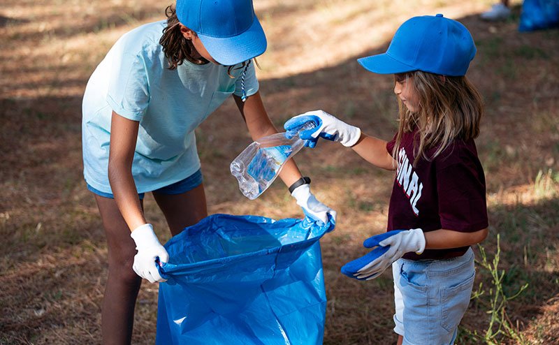 two kids putting plastic bottle in recycle blue bag